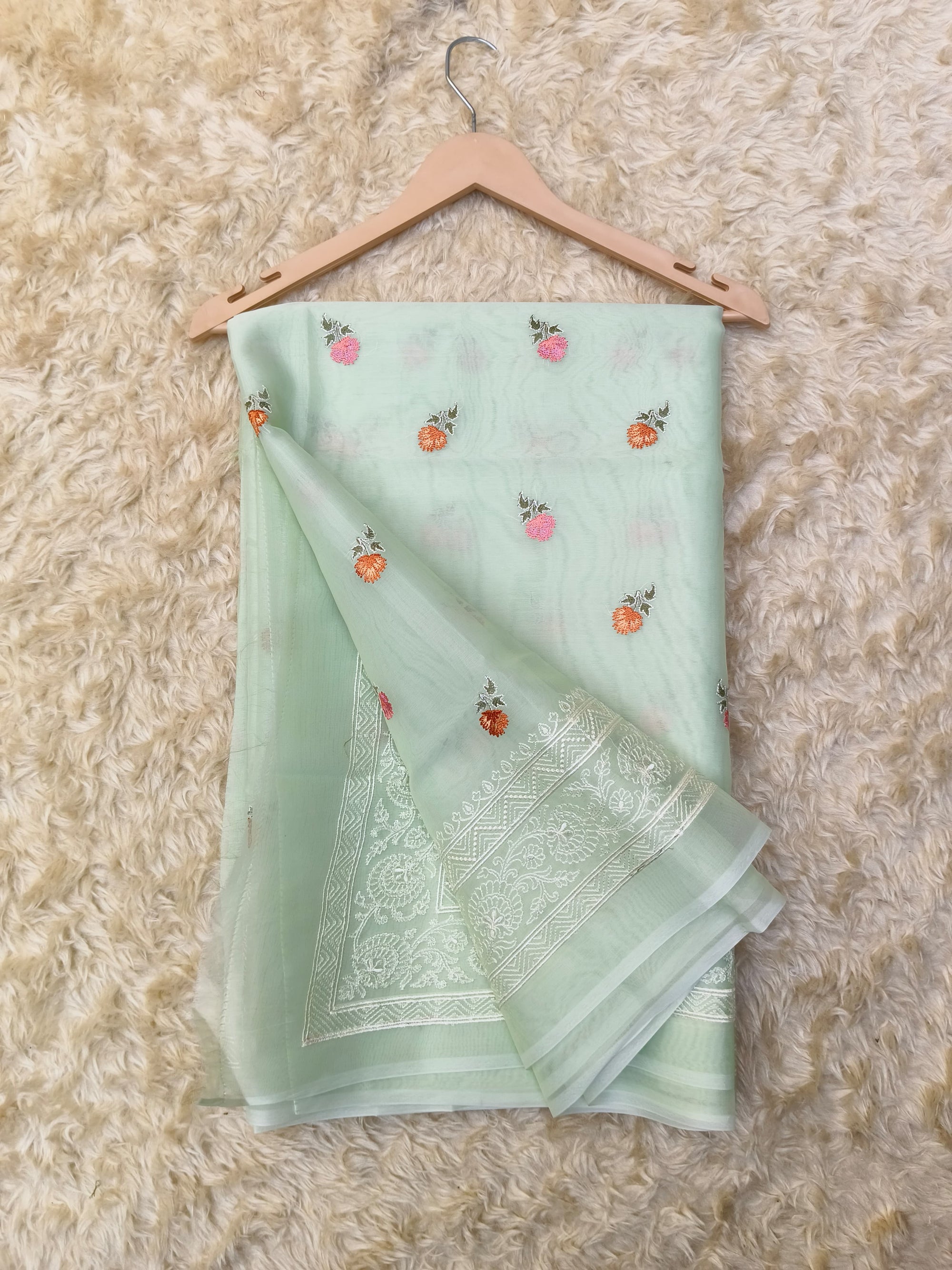 Light green saree with floral patterns on a beige textured surface