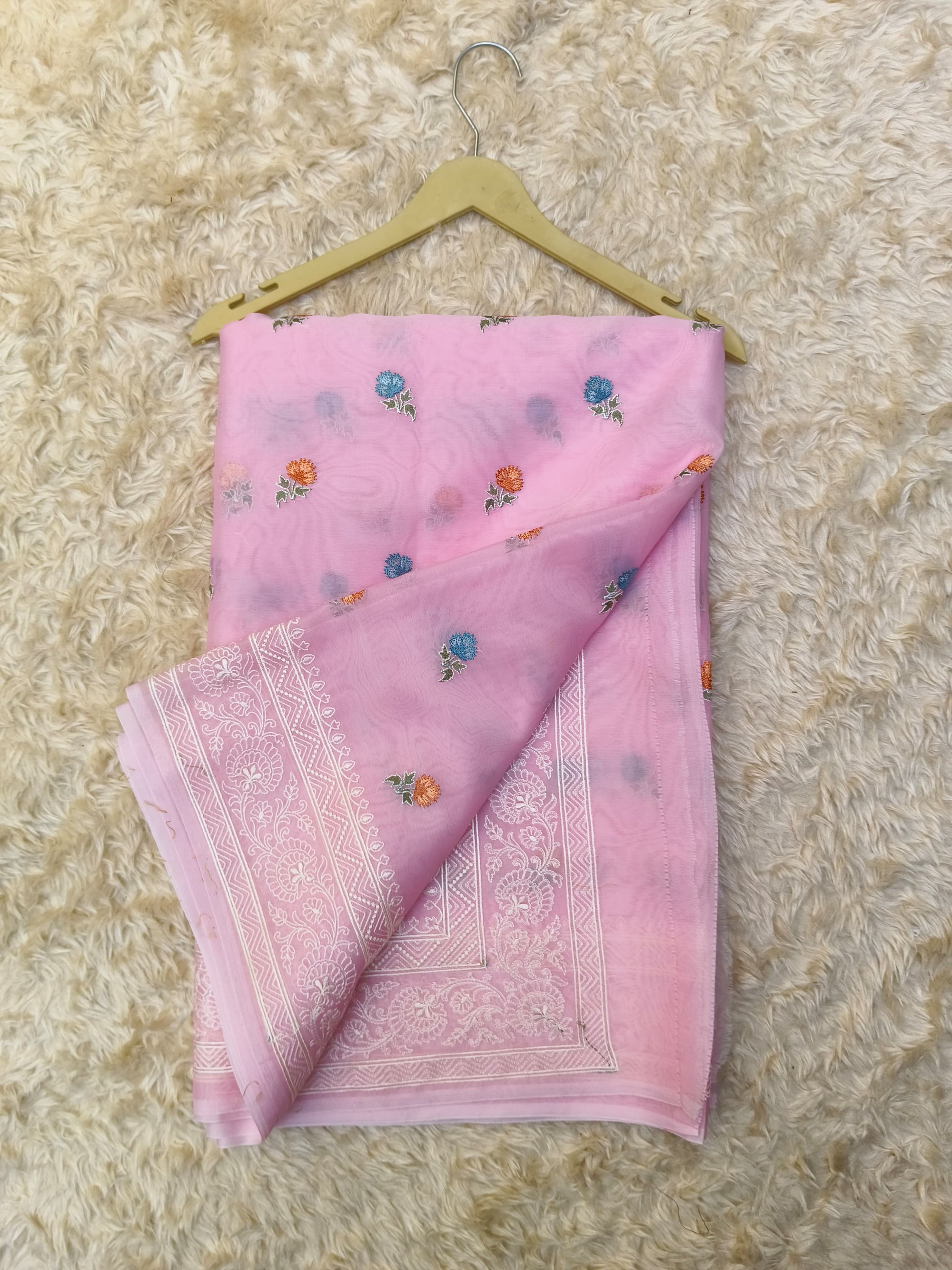 Pink saree with floral patterns and white embroidery on a textured beige surface