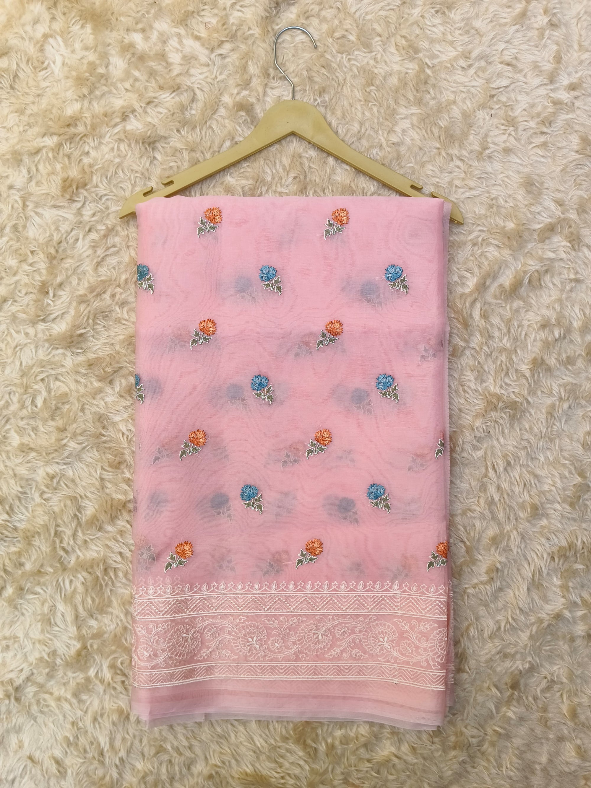 Pink saree with floral patterns on a textured beige surface