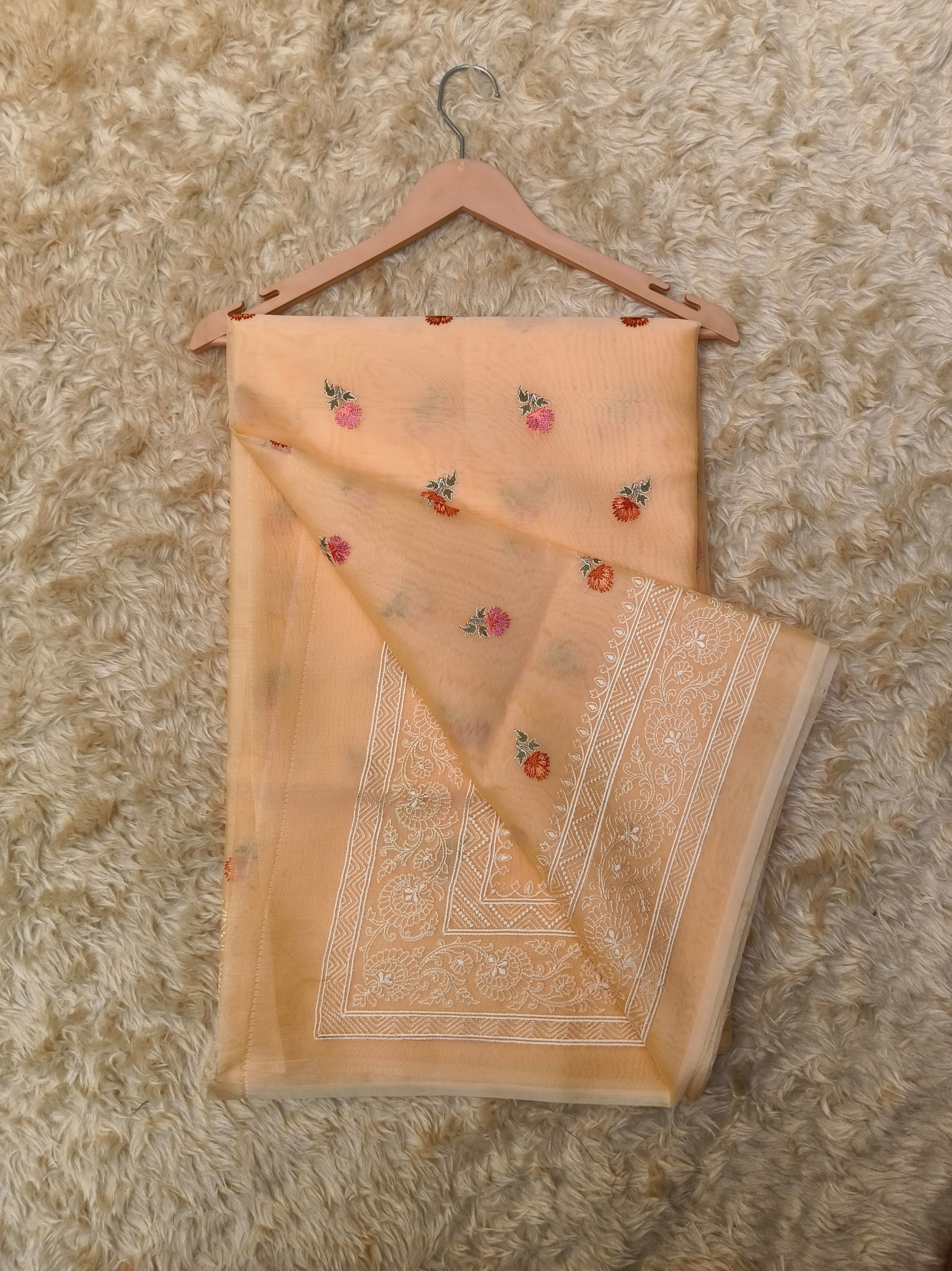 Embroidered peach saree with floral patterns on a textured surface