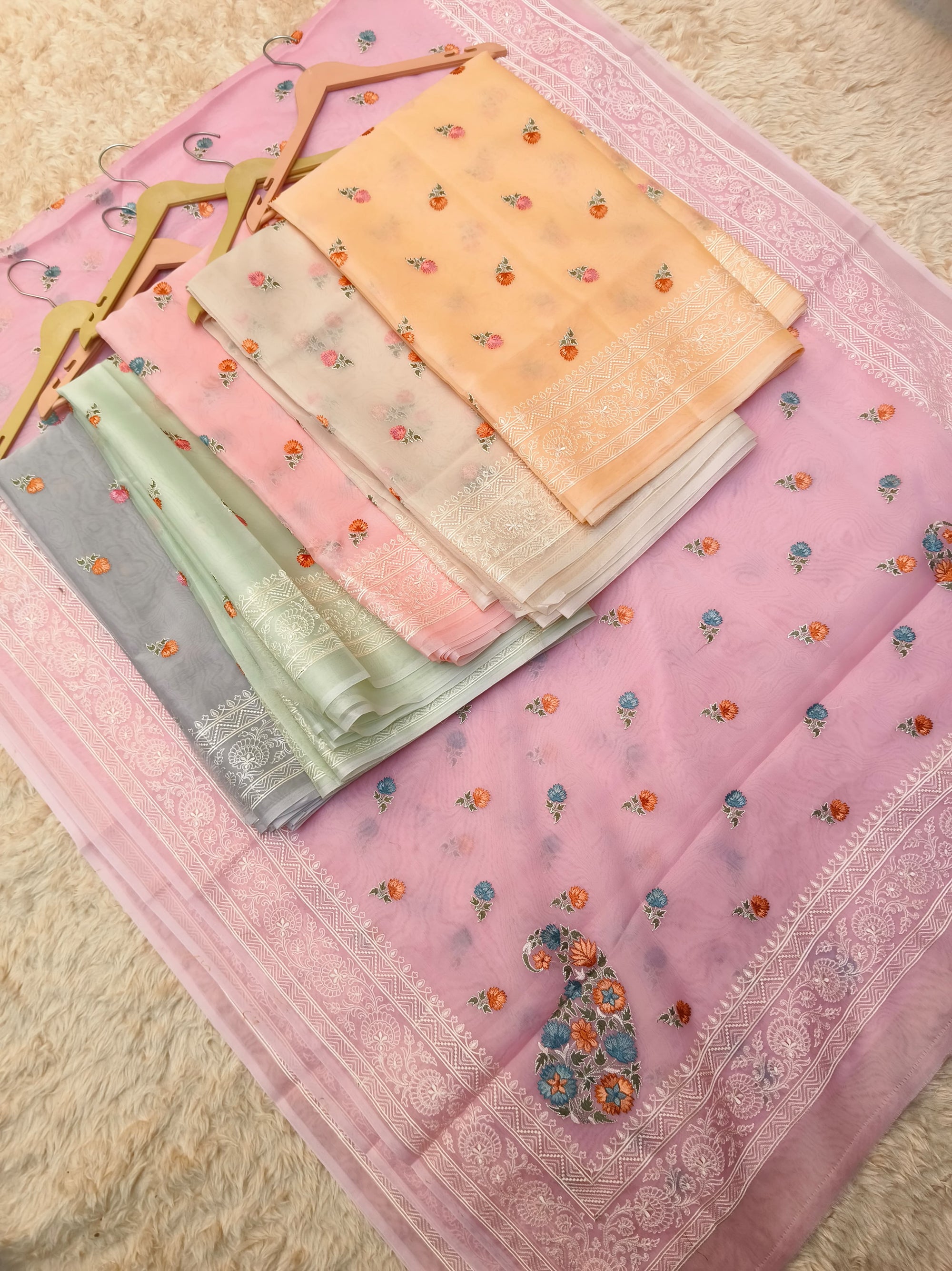 Set of folded saree pieces with floral patterns on a textured surface