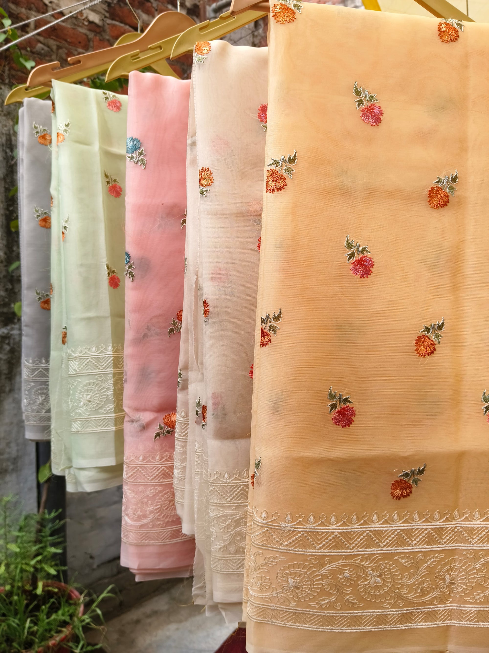 Set of embroidered sarees in various colors hanging on a rack outdoors.