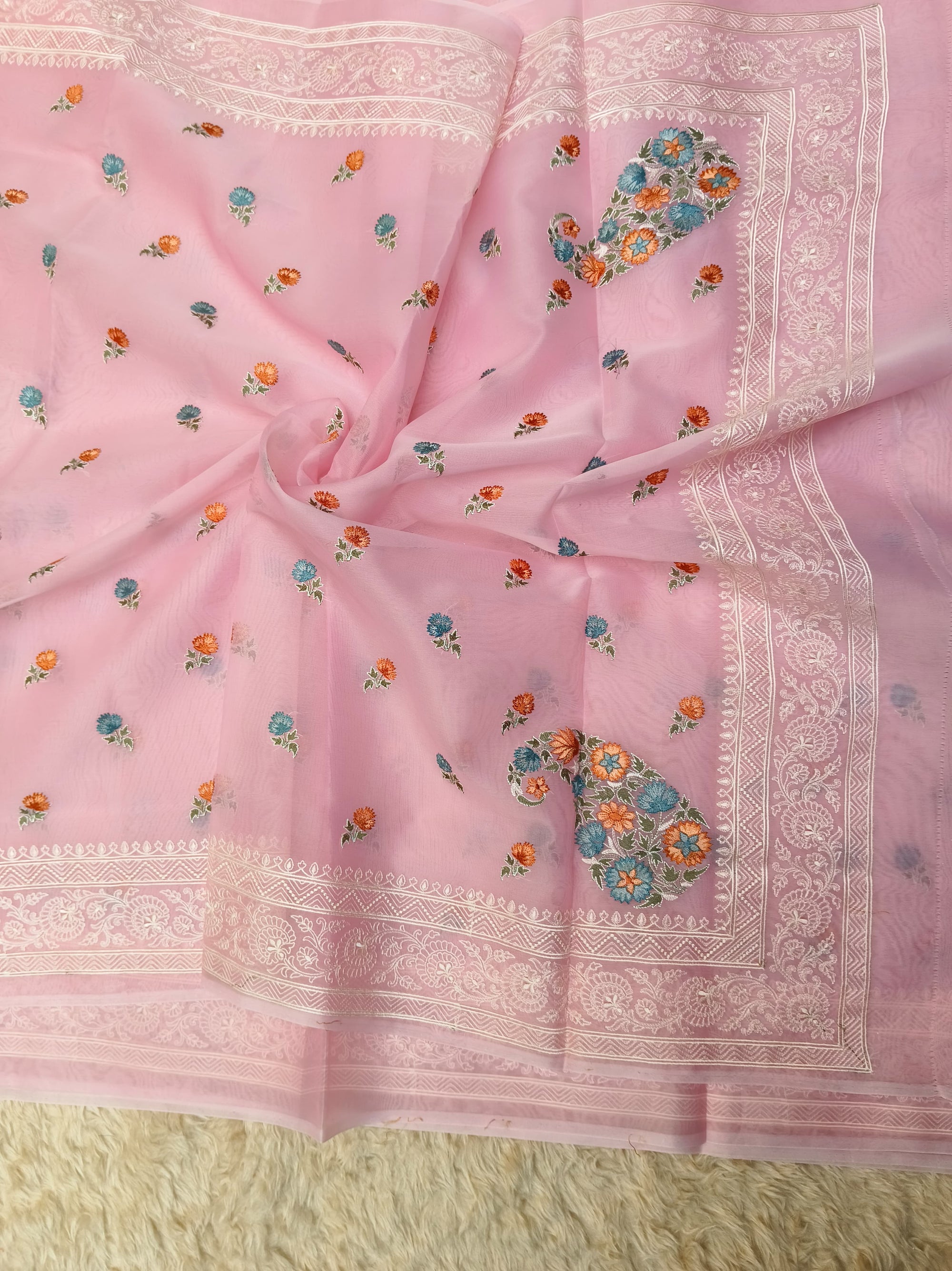 Pink saree with floral patterns and white border on a textured surface
