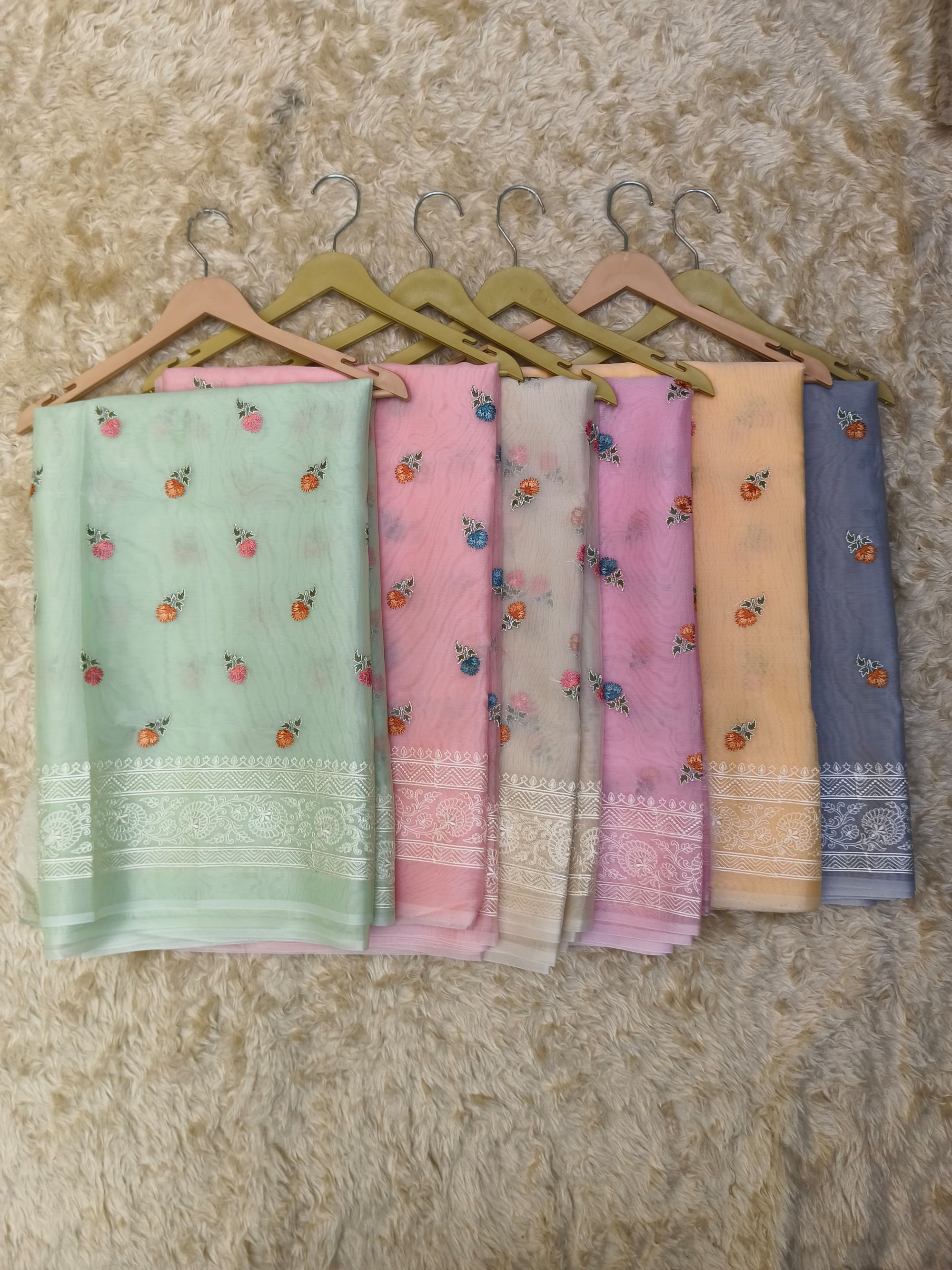 Set of six saree in various colors hanging on a textured wall.