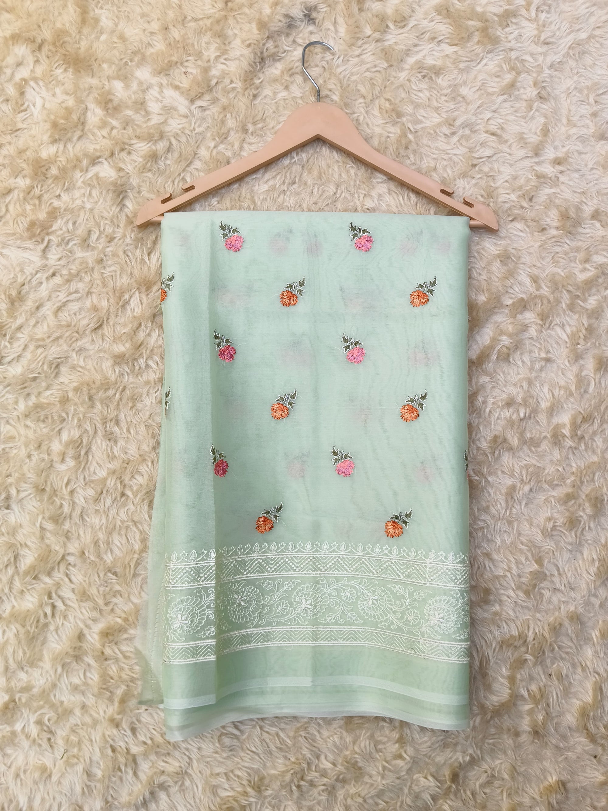 Light green saree with floral patterns on a beige hanger against a textured beige background