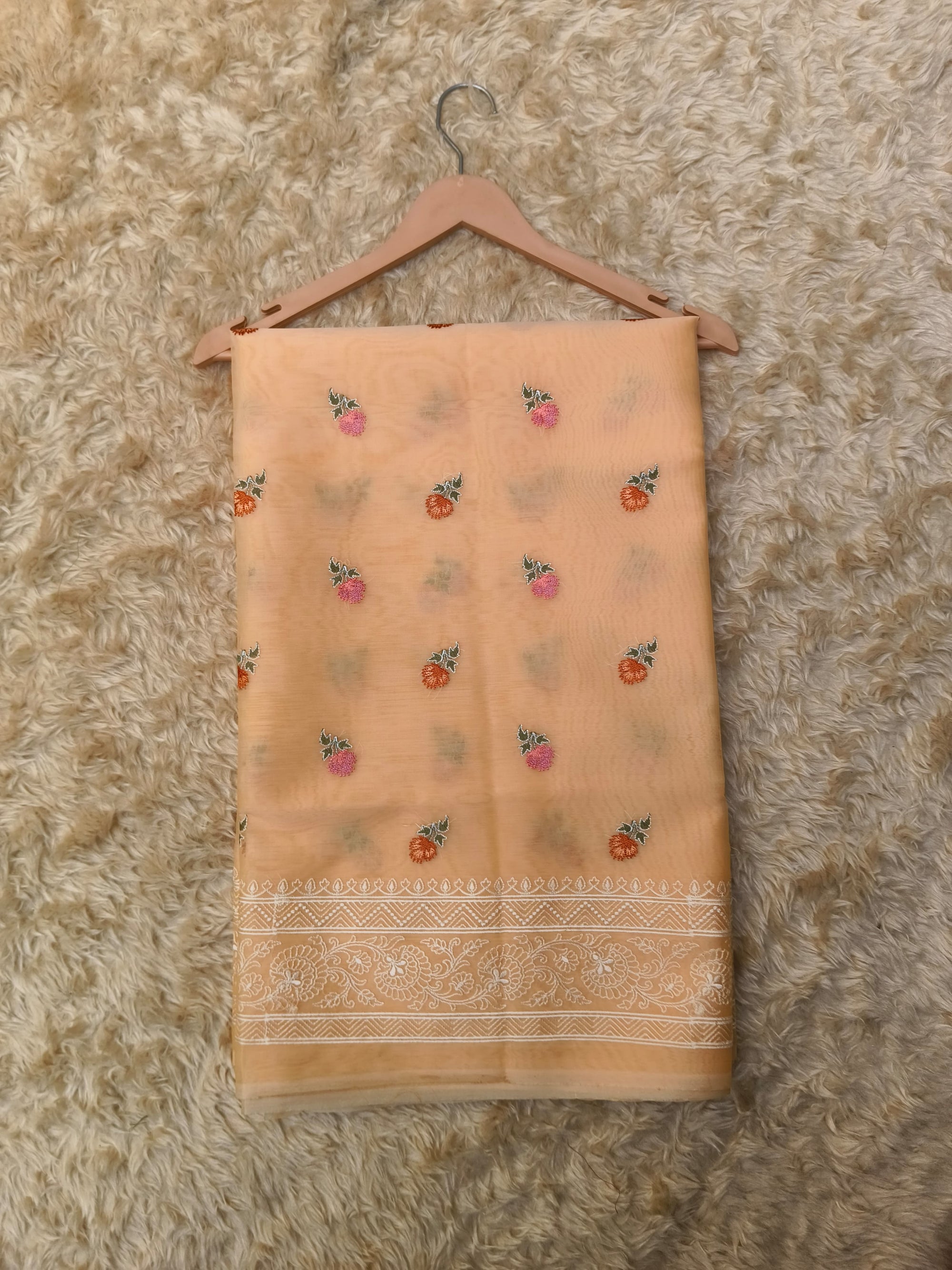 Folded peach-colored saree  with floral patterns on a textured surface