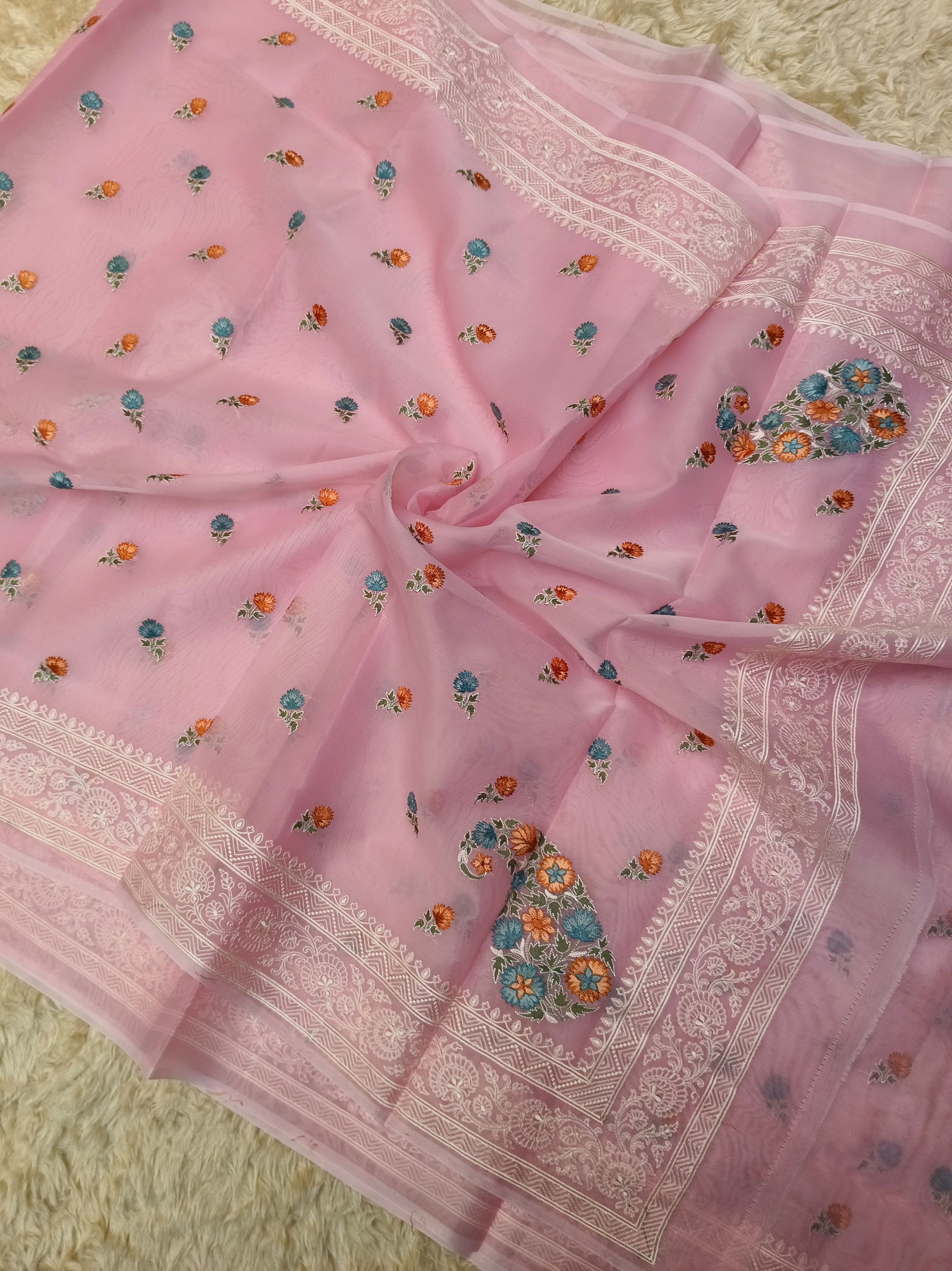 Pink saree with floral patterns and white border on a textured surface