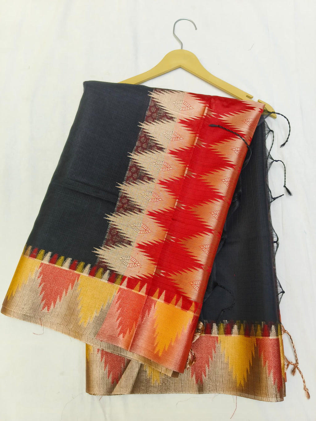 Black saree with red and yellow pattern draped over a hanger against a white background